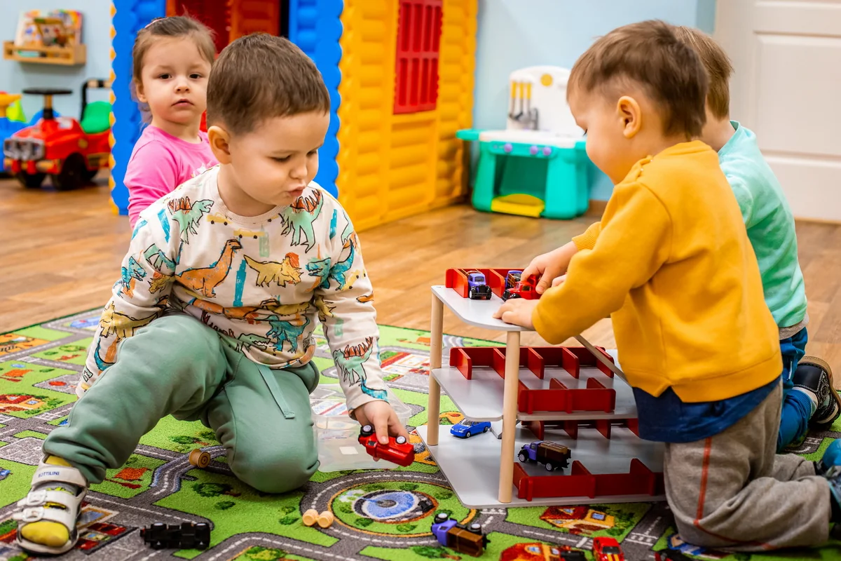 Малыши вместе играют с машинками и игрушечным гаражом